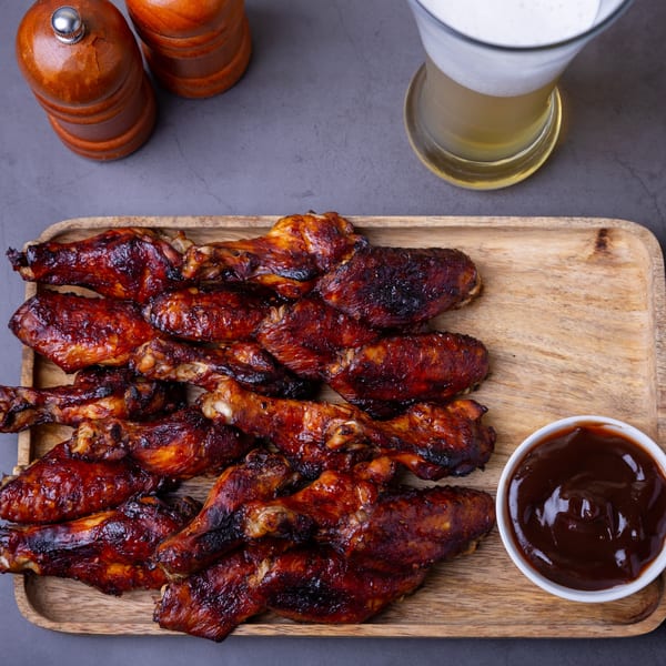 Sammy Sue's BBQ chicken wings with sauce and a beer on a wooden tray.