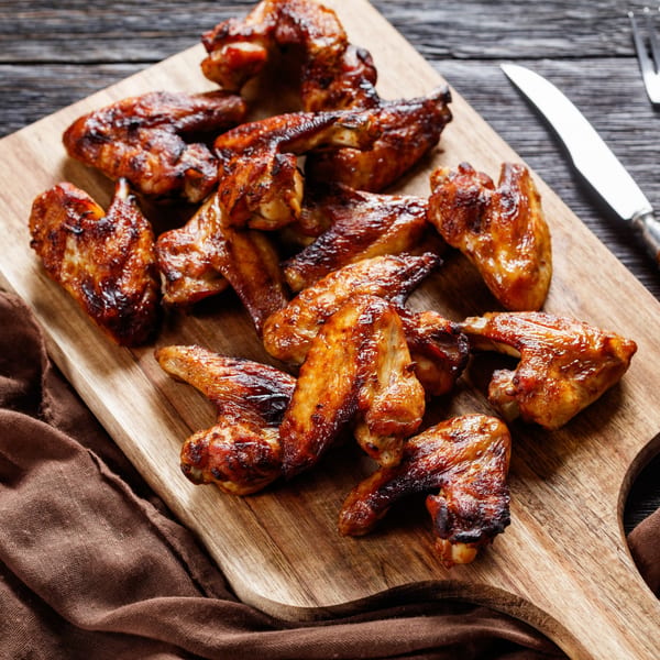 A pile of Sammy Sue's BBQ chicken wings, glistening with sauce, on a wooden cutting board.